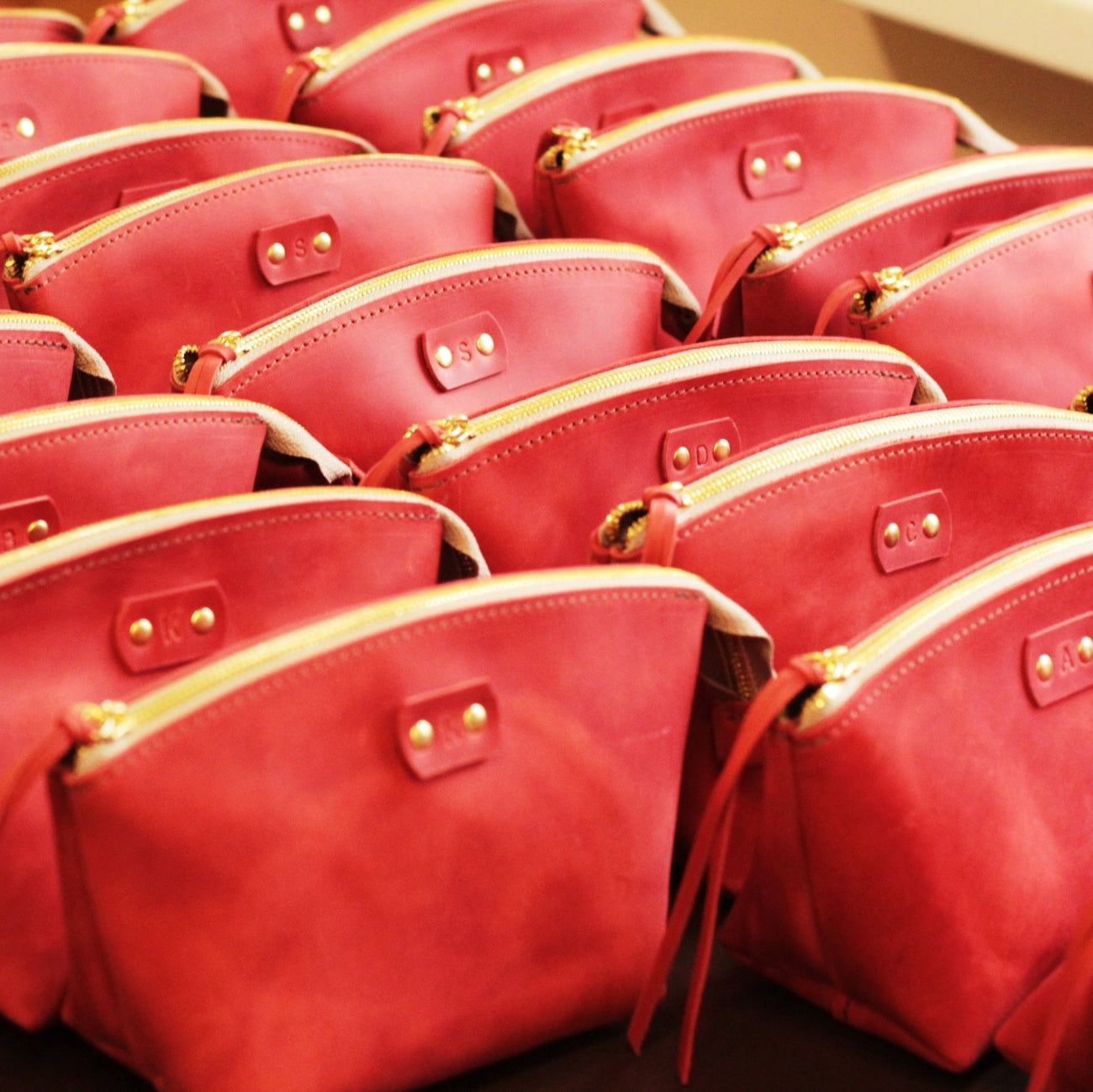 Różne kolory personalizowanych kosmetyczek (czarny, bordowy, cognac) ustawione w rzędzie.