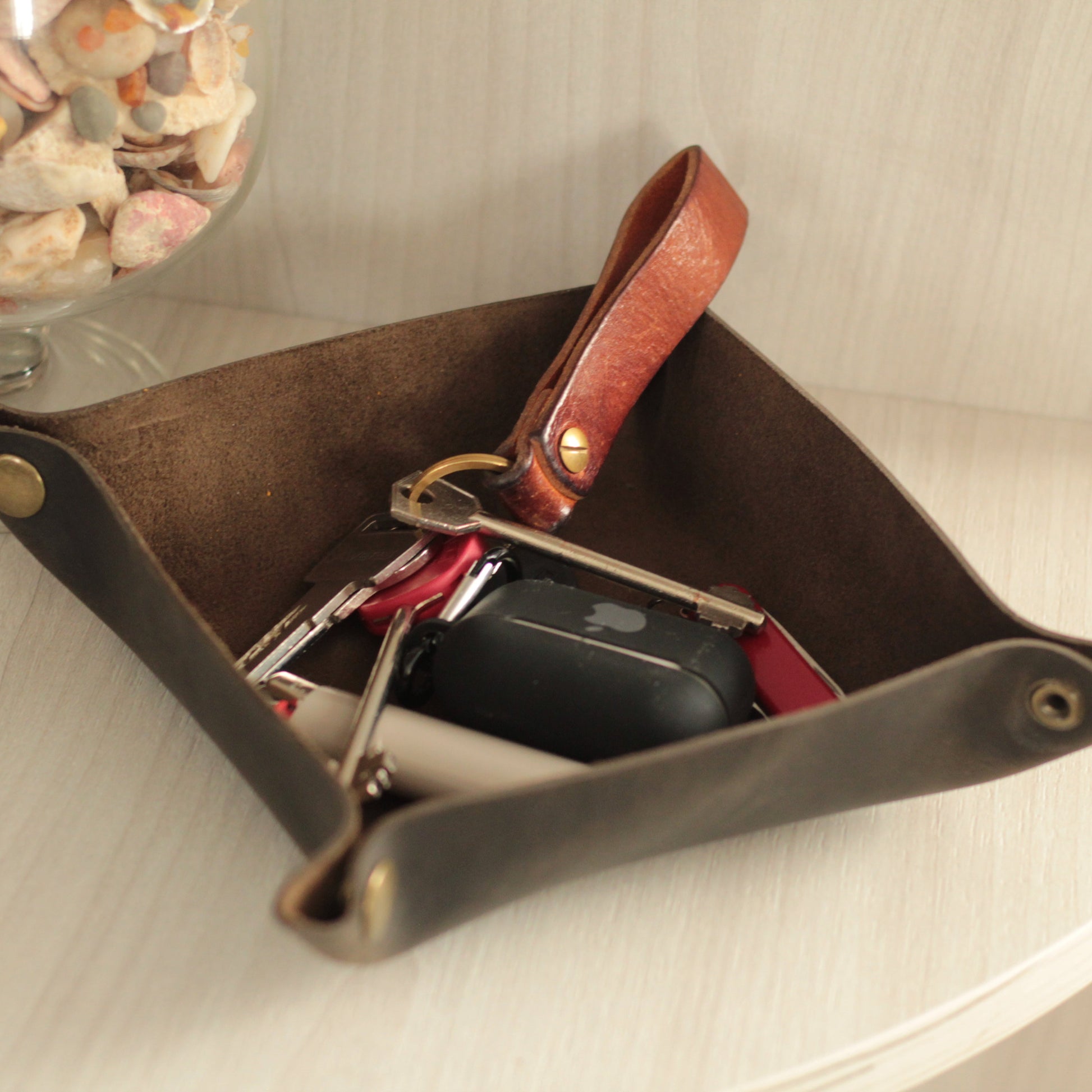 Elegancka podkładka-organizer z skóry z widocznym, trwałym nadrukiem ogniowym (inicjały "AB" i data "2024"). Na niej leżą klucze, obrączka i zegarek, demonstrując zastosowanie.