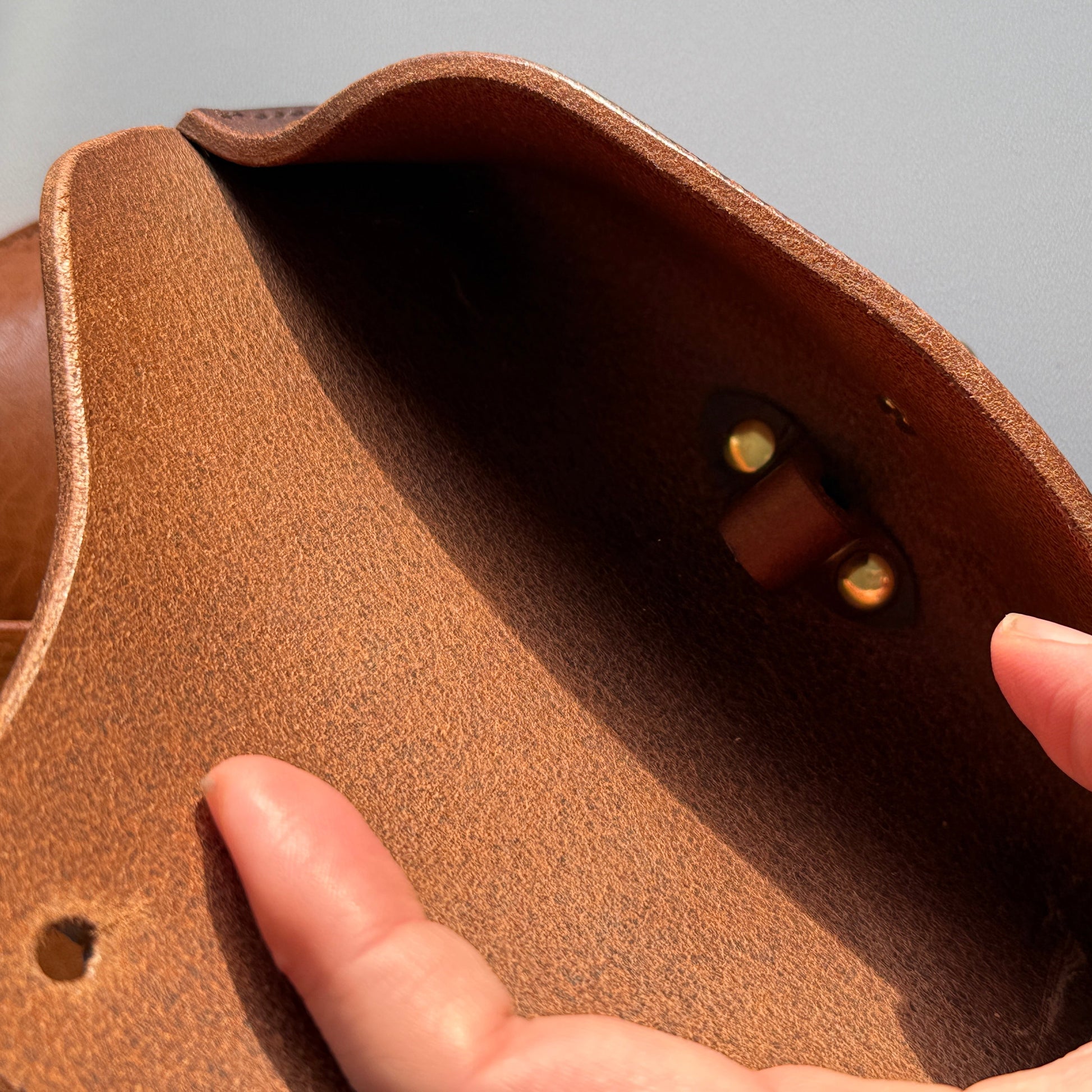 Brązowy, prostokątny futerał na okulary o wymiarach 17.5 x 7.5 cm, uszyty z grubej włoskiej skóry garbowanej roślinnie z widocznym ściegiem i zapięciem na klapę.