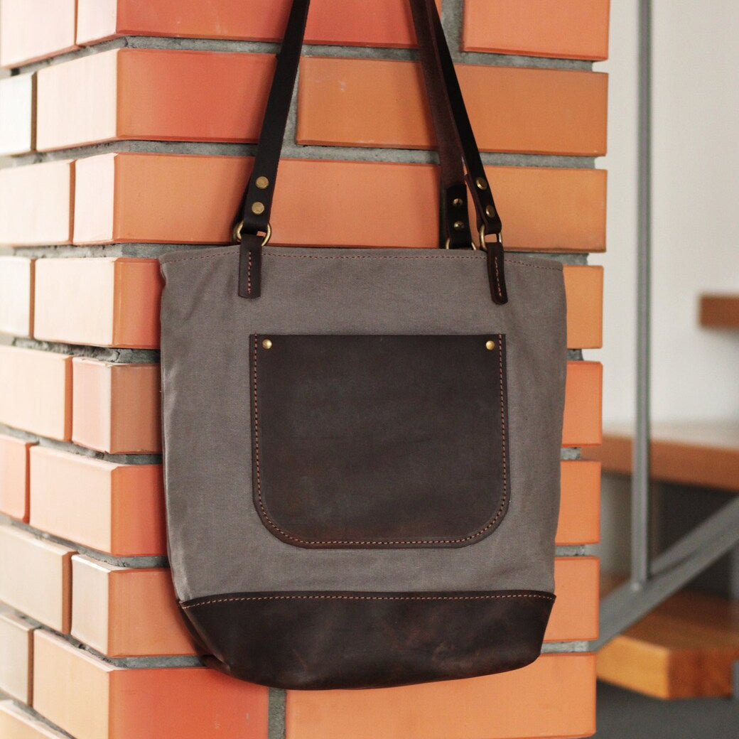 Dłoń trzymająca krótkie, skórzane uchwyty torby o długości 20 cm.

