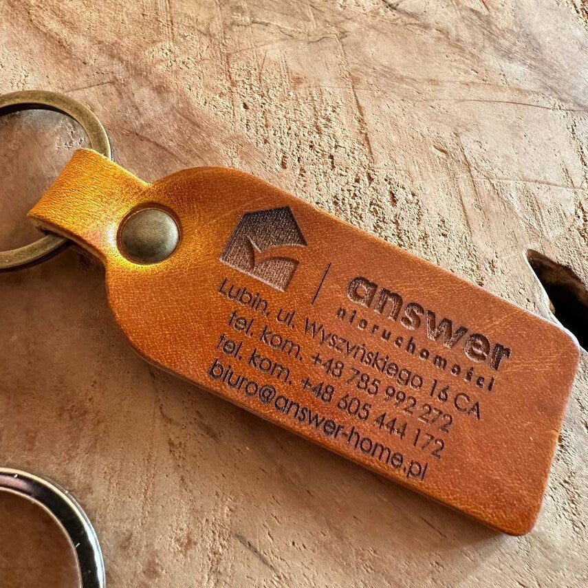 Prezentacja ślubna: brelok na tle obrączek i zaproszenia weselnego

