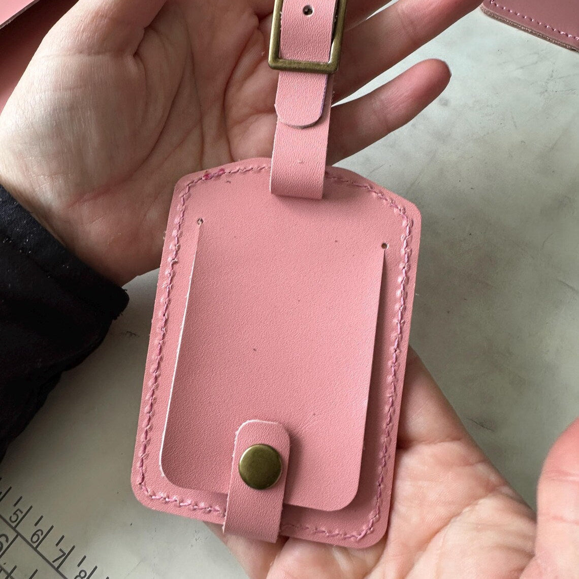 Walizka na lotniskowej karuzeli z widoczną, wyróżniającą się skórzaną zawieszką z inicjałami.

